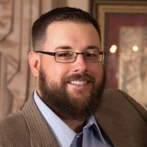 A man with a beard and glasses in a suit.