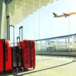 Two red suitcases are near a window and an airplane.