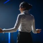 A woman in white shirt holding something while standing on stage.