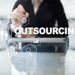 A person is sitting at a table with an arrow pointing to the word outsourcing.