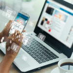 A person is using their phone while sitting at a laptop.