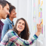 Three people are writing on a wall with sticky notes.