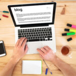 A person typing on a laptop with many pens and pencils around it