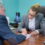 A woman in glasses and suit sitting at a table with an older man.